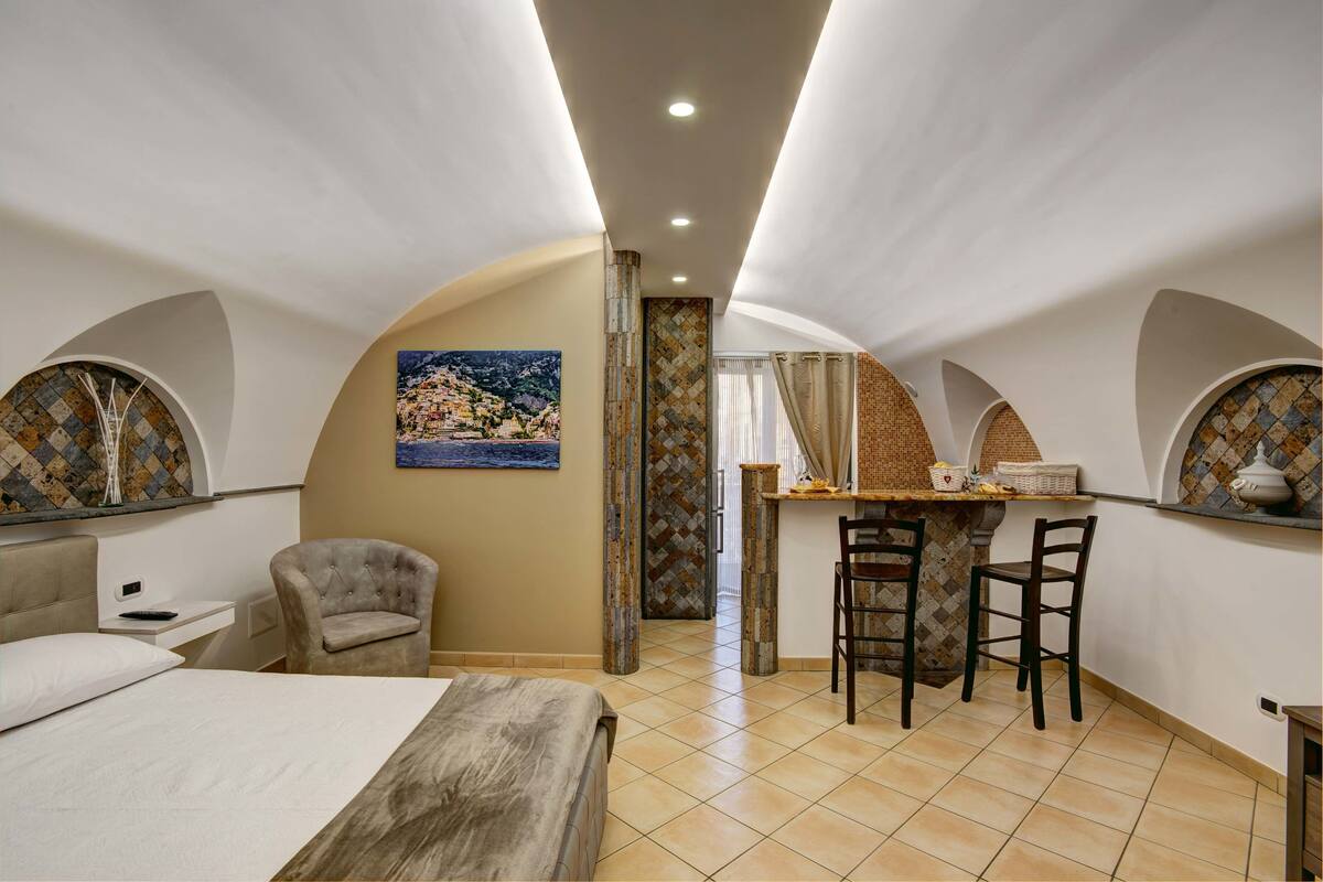 Een slaapkamer met een bed, een bureau en twee stoelen. Er hangt een schilderij aan de muur en er is een raam met gordijnen.