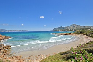 Una playa costera con aguas cristalinas, costa rocosa y una montaña al fondo.