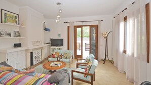 Een woonkamer met een bank, fauteuils, een salontafel, een televisie en een open haard.