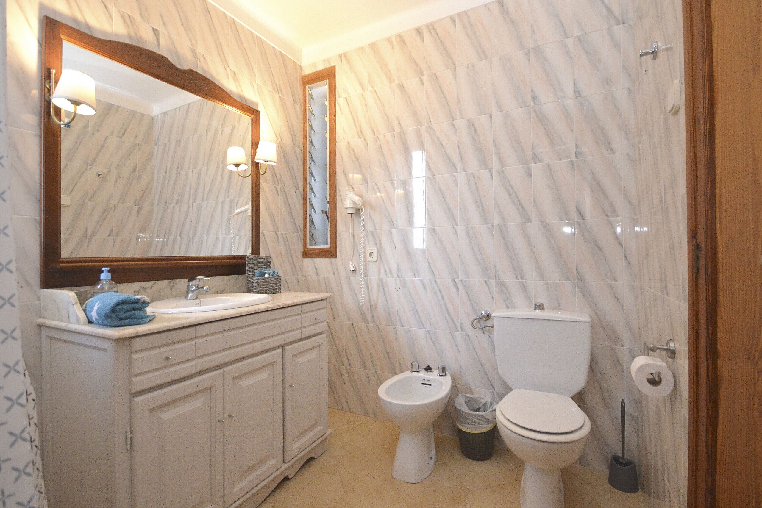 Een badkamer met een marmeren vloer, een wastafel, een bidet, een toilet, een spiegel en een prullenbak.