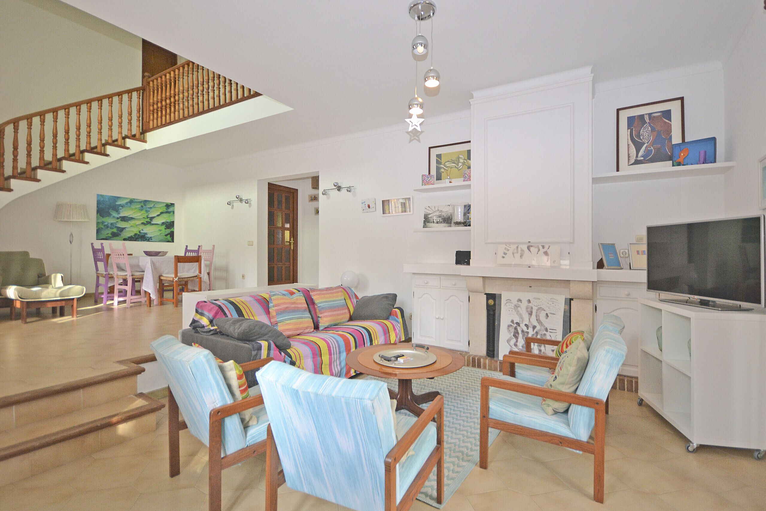 A spacious living area with a staircase, a sofa set, a television, and a kitchen area.