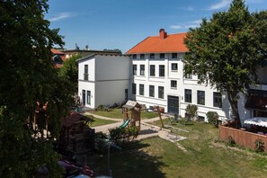 Une cour avec un terrain de jeux, un bâtiment blanc avec un toit rouge et une maison de jeu en bois.
