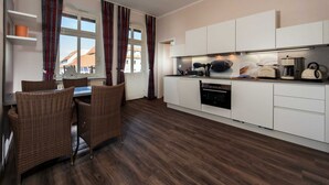 A modern kitchen with white cabinets, a dining area with wicker chairs, and a window with curtains.
