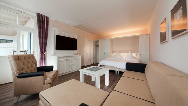 A modern hotel room with a sofa, armchair, and a flat-screen TV.