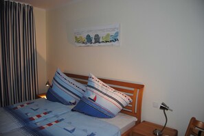Uma cama bem arrumada com roupa de cama listrada, um quadro na parede de cadeiras coloridas e um abajur.