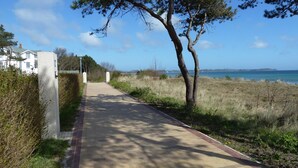 Ein gepflasterter Weg führt zu einem weißen Gebäude, im Hintergrund ist ein Leuchtturm zu sehen.