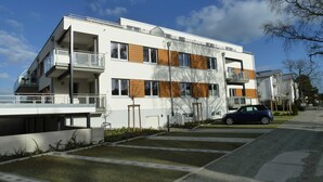 Ein modernes Mehrfamilienhaus mit Balkonen, ein Auto auf der Einfahrt und ein klarer Himmel.