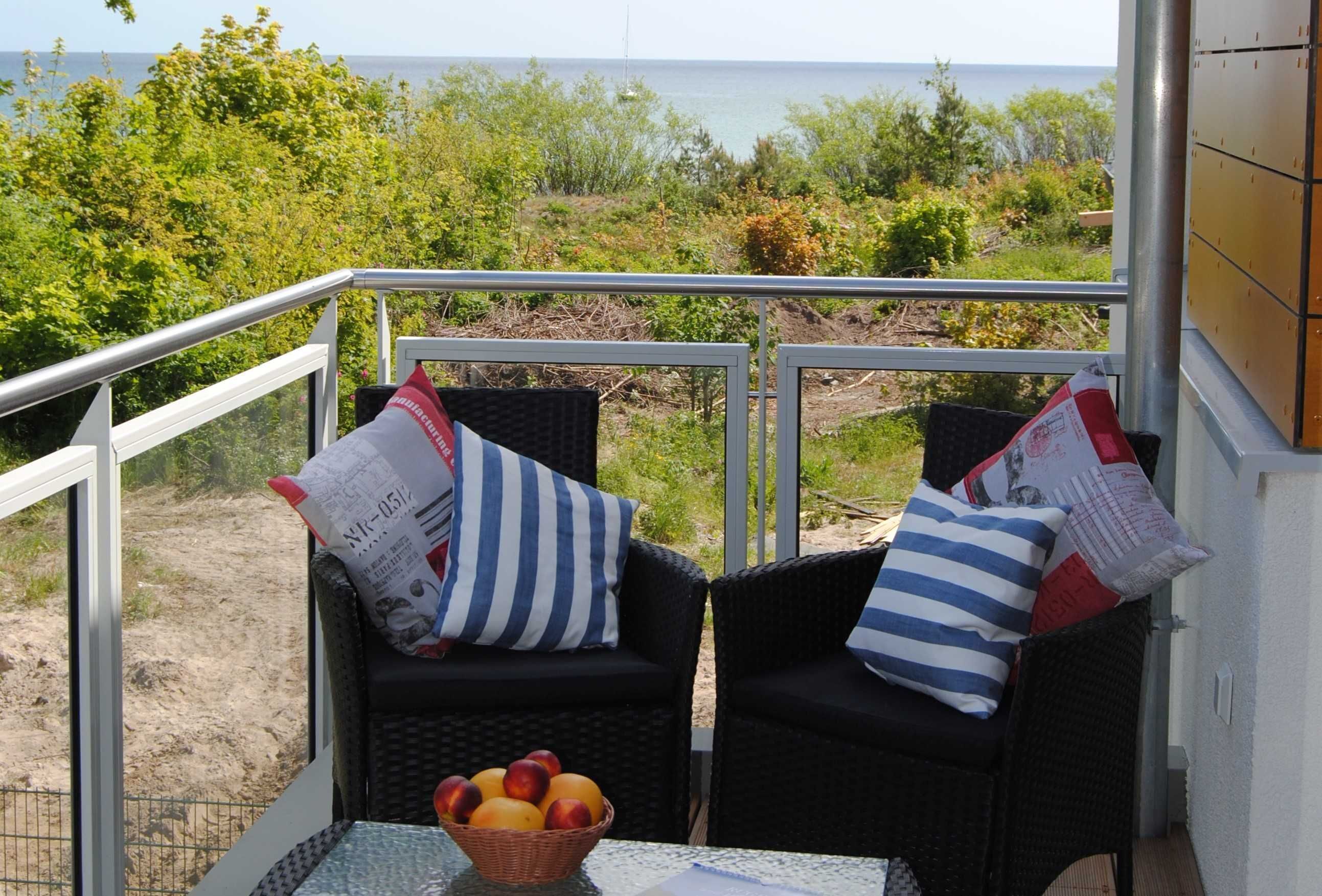 Un balcón con sillas de mimbre, una mesa con fruta y vista al mar.