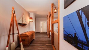 Um corredor com piso de madeira, um banco de madeira, uma decoração de barco à vela fixada na parede e um quadro com um navio.