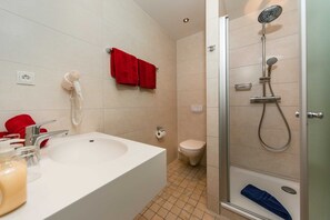 Une salle de bain avec un lavabo blanc, des serviettes rouges, des toilettes et une douche.