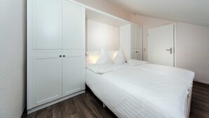 Ein Schlafzimmer mit großem Kleiderschrank, einem Bett mit weißer Bettwäsche und einer Tür mit Spiegel.