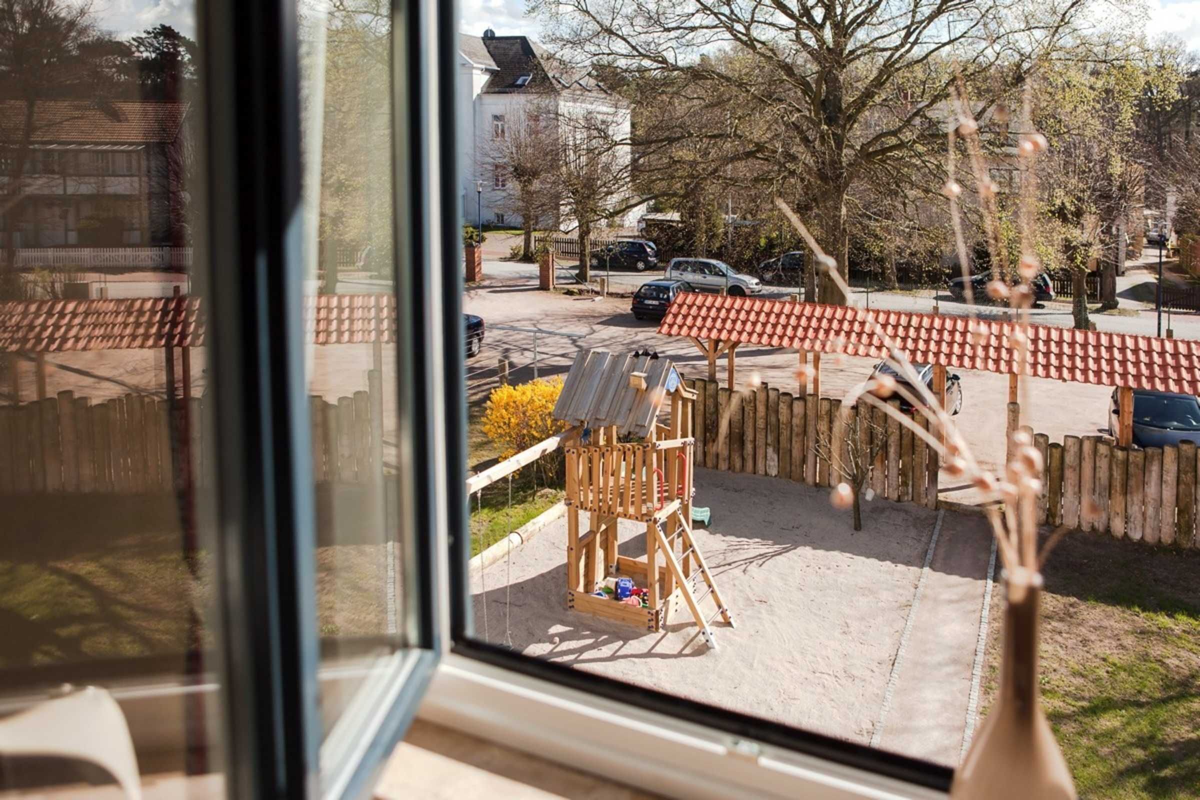 A view from a window overlooking a playground with a wooden structure and sand.
