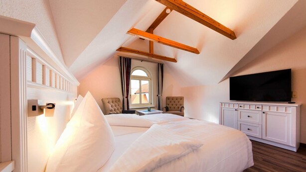A bedroom with a large bed, a TV, and a wooden ceiling beam.