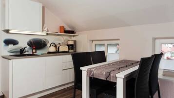 Cocina compacta con armarios blancos, cafetera y comedor con mesa y sillas.