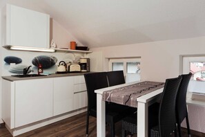 Une cuisine compacte avec des meubles blancs, une machine à café et un coin repas comprenant une table et des chaises.