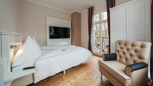 Ein Schlafzimmer mit Bett, Wandfernseher, Sofa und einem Fenster mit Vorhängen.