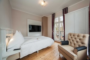 Une chambre à coucher avec un lit, un téléviseur fixé au mur, un canapé et une fenêtre avec des rideaux.