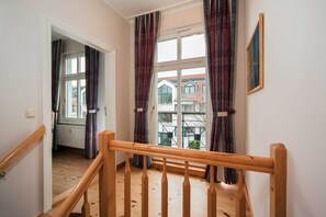 A staircase with wooden railings leading to a room with a window, curtains, and a radiator.