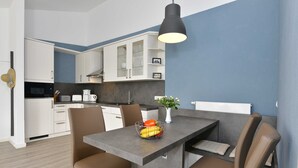 Cozinha moderna com armários brancos, micro-ondas e cafeteira. Possui uma área de jantar com mesa e cadeiras, e um vaso com flores sobre a mesa.