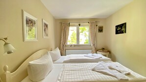 A hotel room with two beds, a window with curtains, a bedside table with a lamp, and framed pictures on the wall. - House Nemo, App. 8, Germany (Heringsdorf)