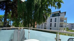 A balcony with a glass table and chairs, overlooking a modern building and trees. - House Nemo, App. 8, Germany (Heringsdorf)