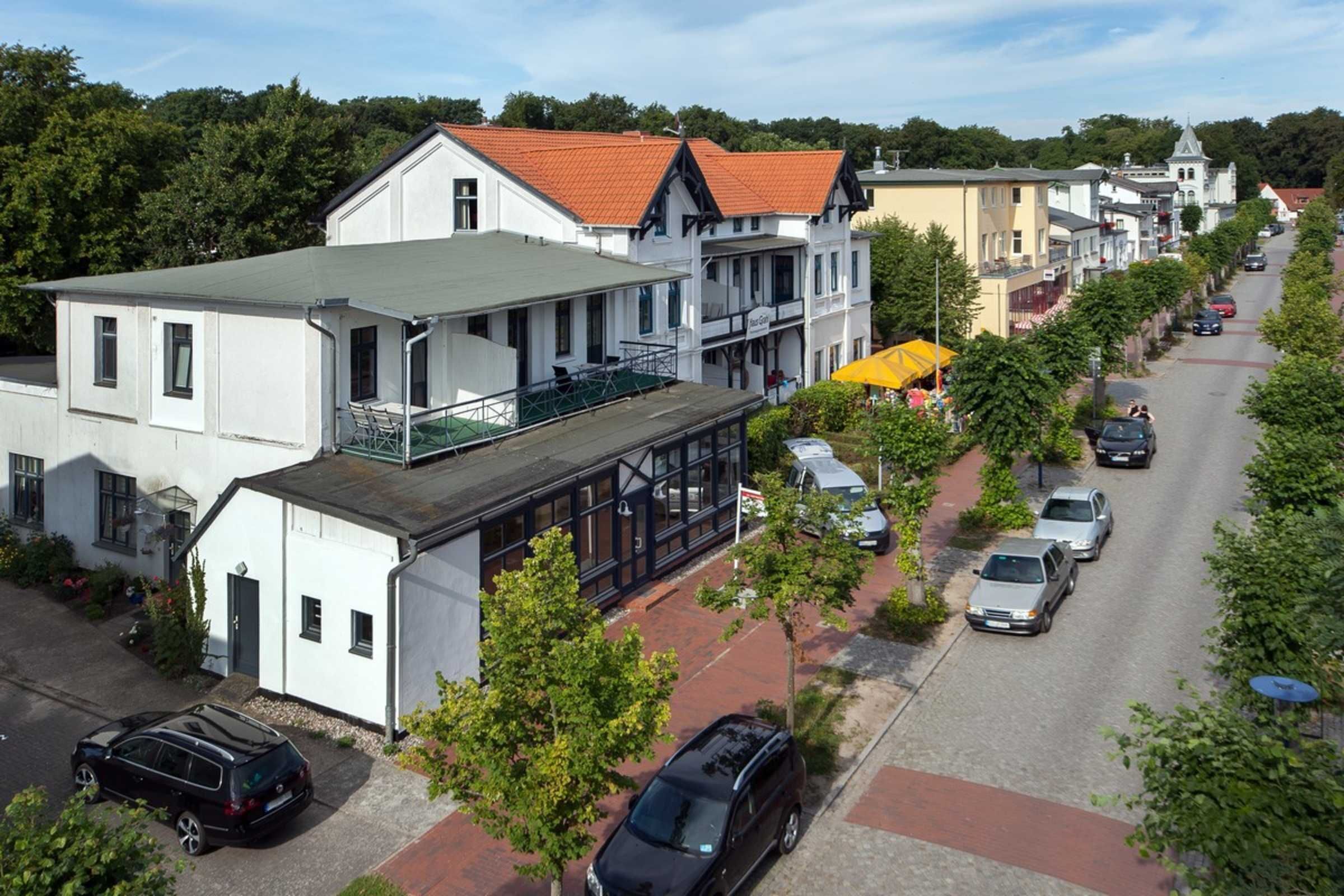 Blick von einer Straße in eine Stadt mit Gebäuden, parkenden Autos und einem Fußweg.
