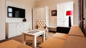 Ett modernt vardagsrum med en platt-TV, en stoppad fåtölj, en soffa, ett bord och en röd golvlampa.