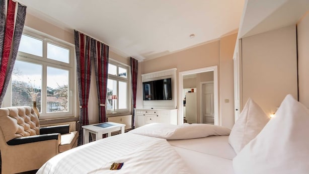 A hotel room with a large bed, a chair, a desk, a television, and a window with curtains. - Holiday home Lauterbach - Haus Grahl GM 69912 (Graal-Müritz)