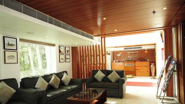 A modern lobby with dark green sofas, a glass coffee table, wooden reception desk, and framed artwork on the walls. - Dfort Hotel Kollam (Kollam)