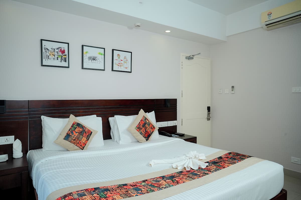A neatly made bed with a white comforter and decorative pillows, a bedside table with a phone and a tissue box, and three framed artworks on the wall above the bed.