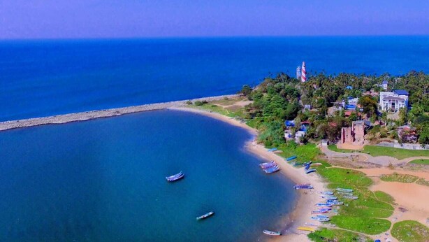 An aerial view of a coastal area with a lighthouse, beach, boats, and a cluster of buildings surrounded by greenery. - Dfort Hotel Kollam (Kollam)