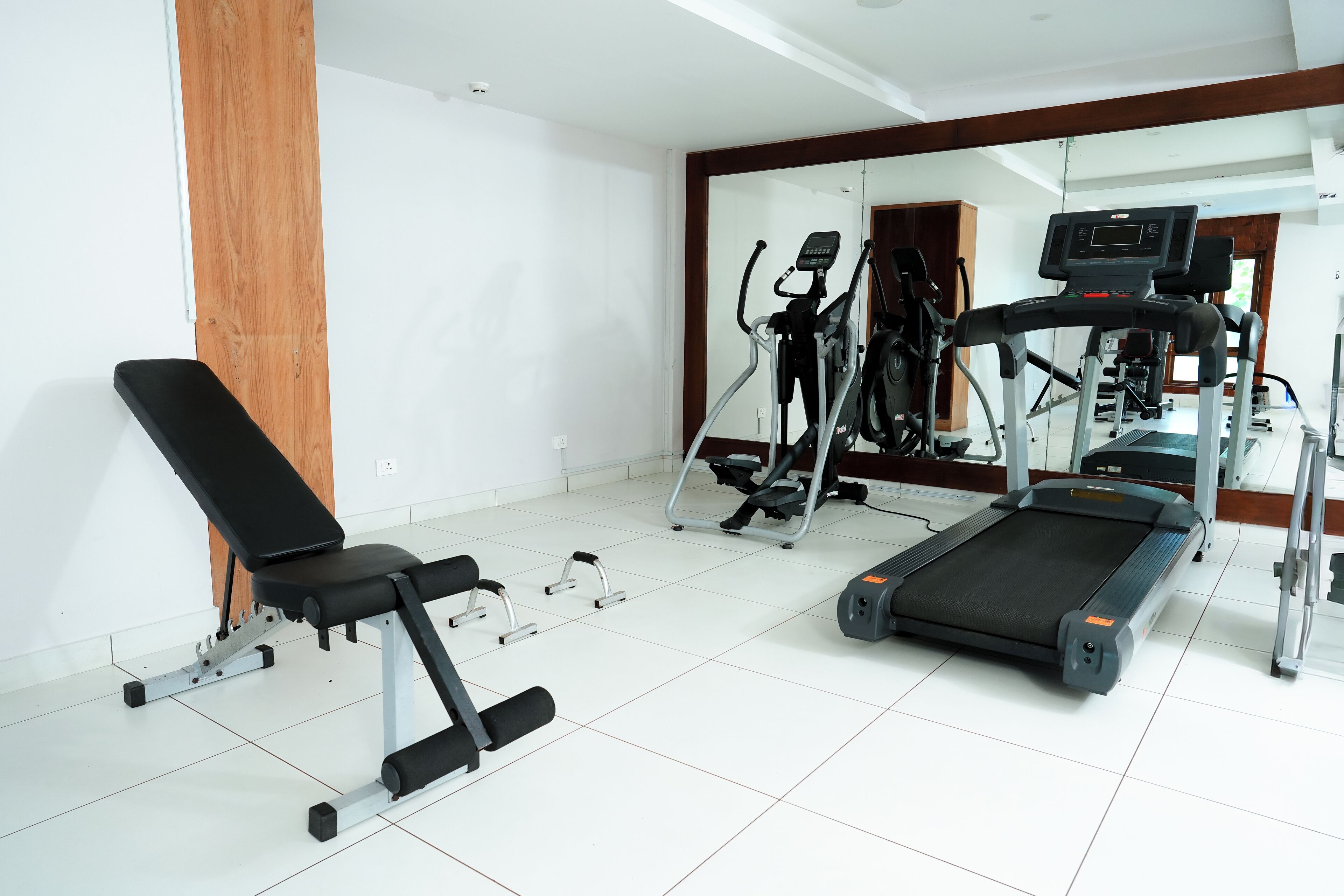 Ein Fitnessraum mit Bank, Ellipsentrainer und Laufband.