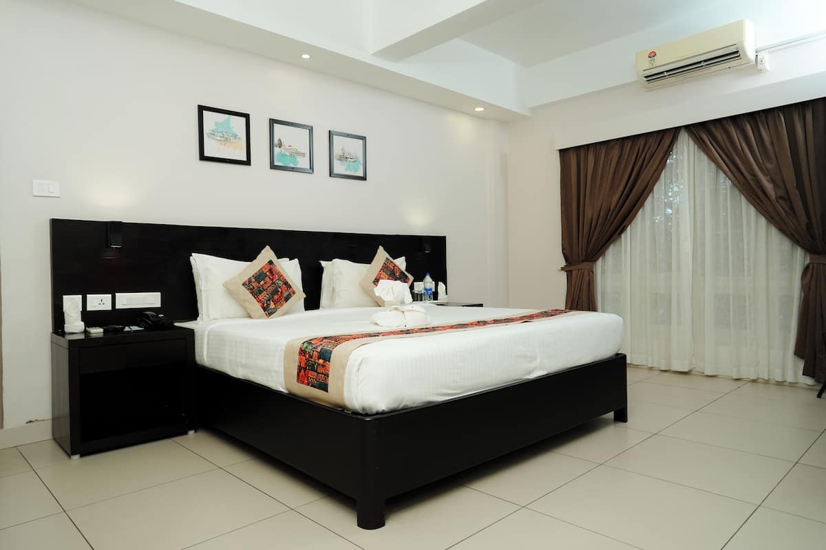 A modern hotel room with a large bed, a nightstand, a wall-mounted air conditioner, and three framed pictures.