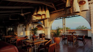 An indoor dining area with wooden tables and chairs, a bar area, and a view through an arched doorway to the outside. - Dfort Hotel Kollam (Kollam)