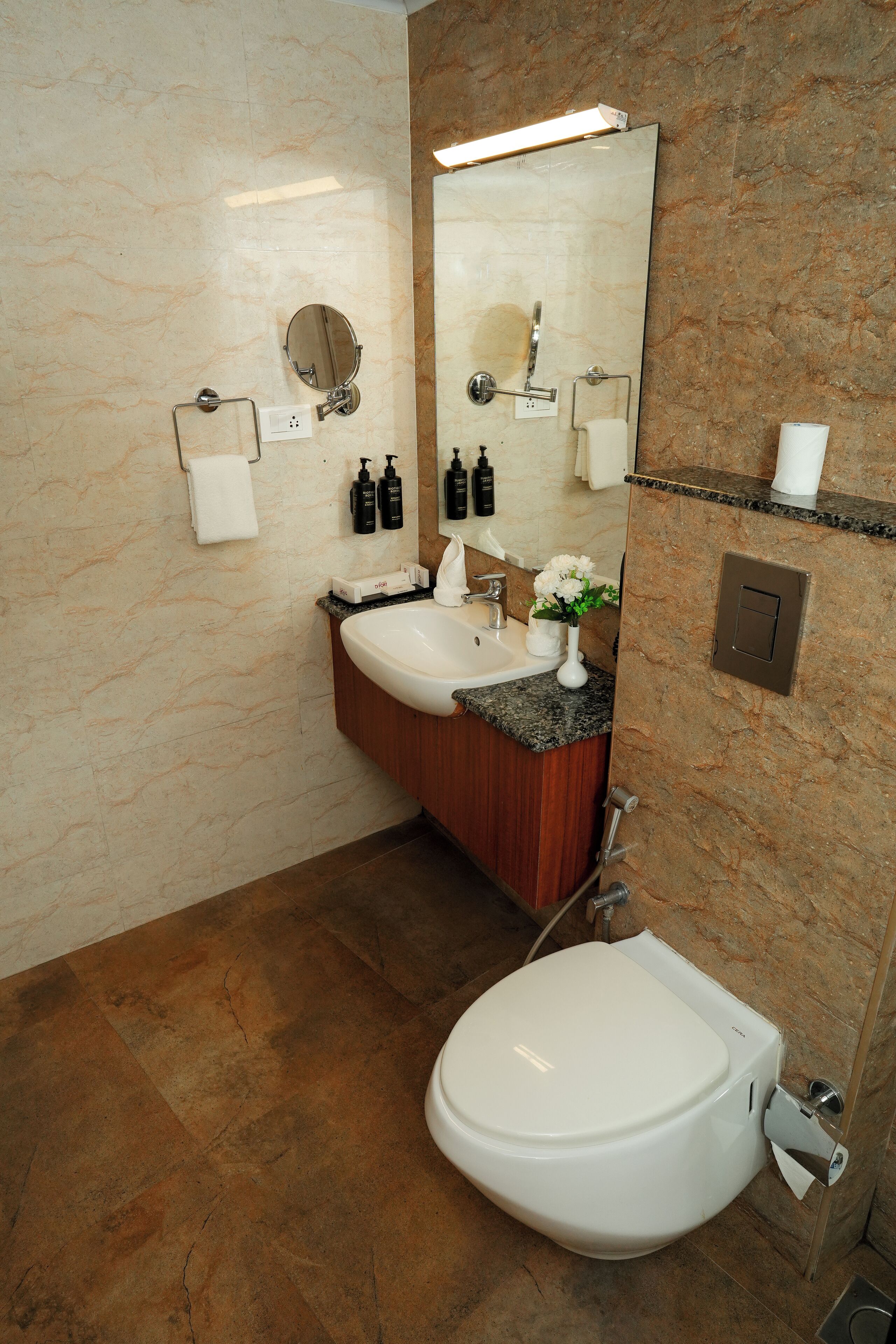 Een badkamer met een marmeren wand, een wastafel met een aanrecht, een toilet en een spiegel.