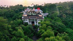 A large, multi-story building surrounded by dense greenery, with a prominent flag on top. - Dfort Hotel Kollam (Kollam)