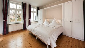 Une chambre à coucher avec un lit double, une armoire blanche et une fenêtre avec des rideaux.