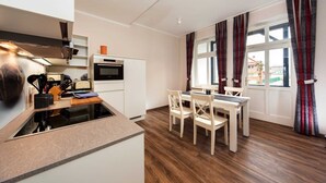 Une cuisine moderne dotée d’un four et d’un micro-ondes encastrés, un coin repas avec une table et des chaises, et de grandes fenêtres avec des rideaux.