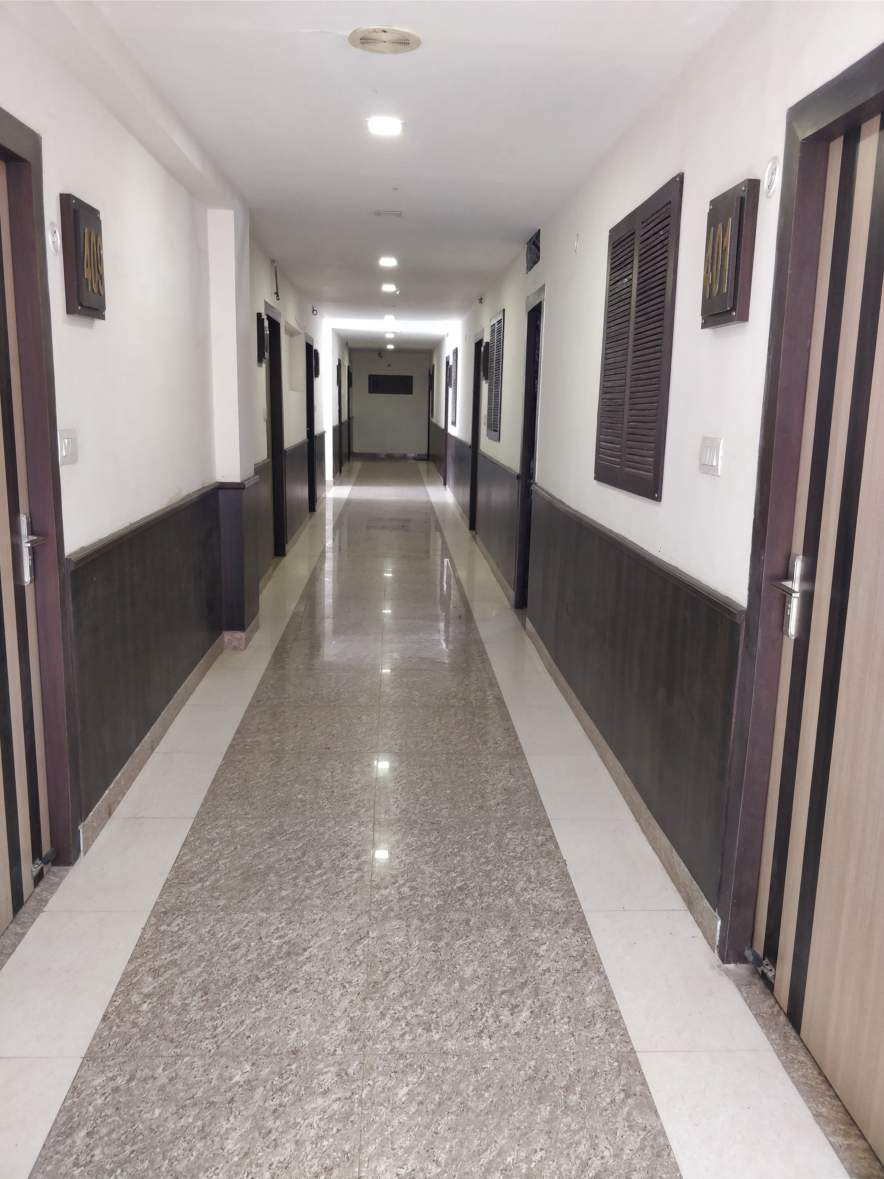A long, narrow hallway with a polished marble floor, flanked by doors and walls with dark and light panels.