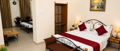 A hotel room with a bed, a desk, a chair, a small table, a lamp, and a painting on the wall.