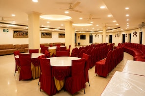 A banquet hall with round tables, red chairs, and a sofa. - Central Hotel (Lucknow)
