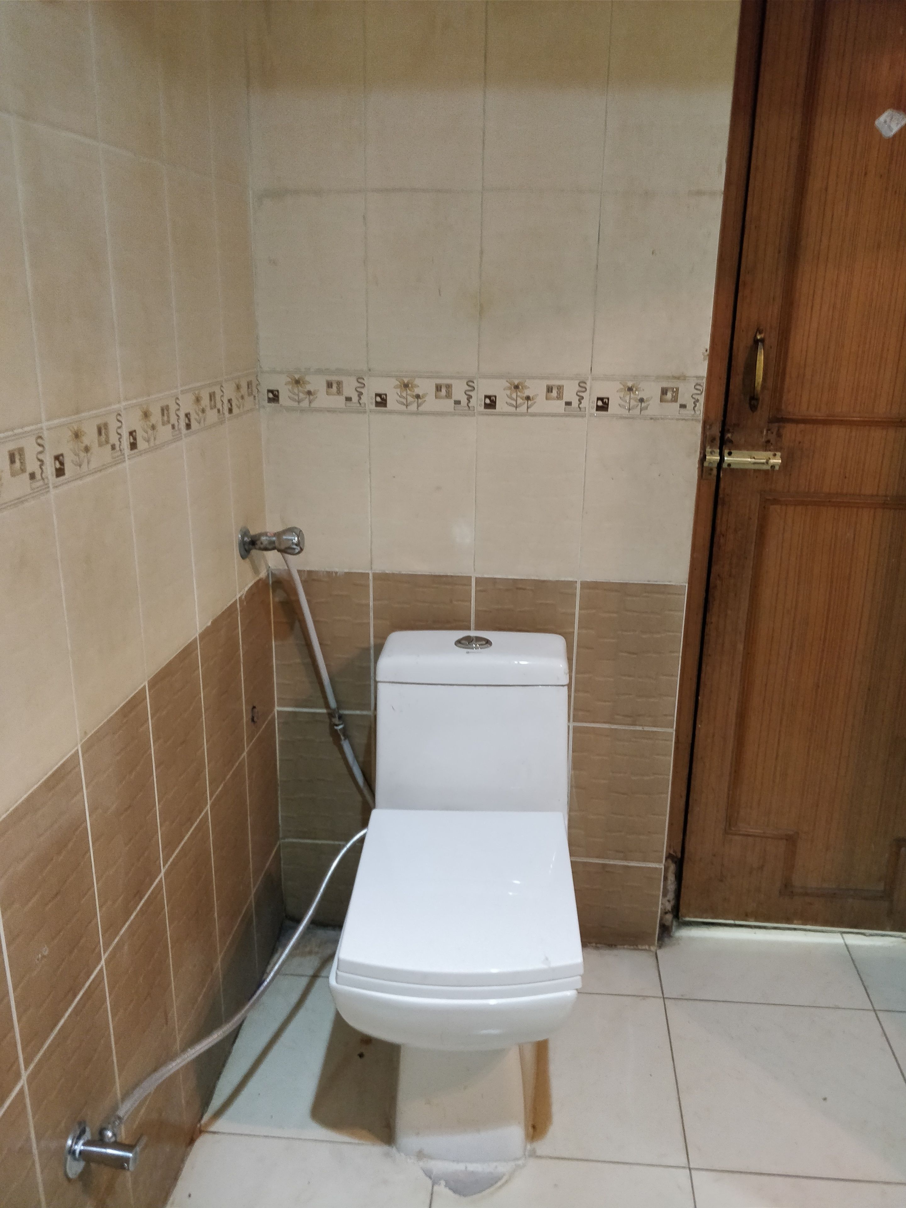 A small, tiled bathroom with a toilet, a shower, and a wooden door.