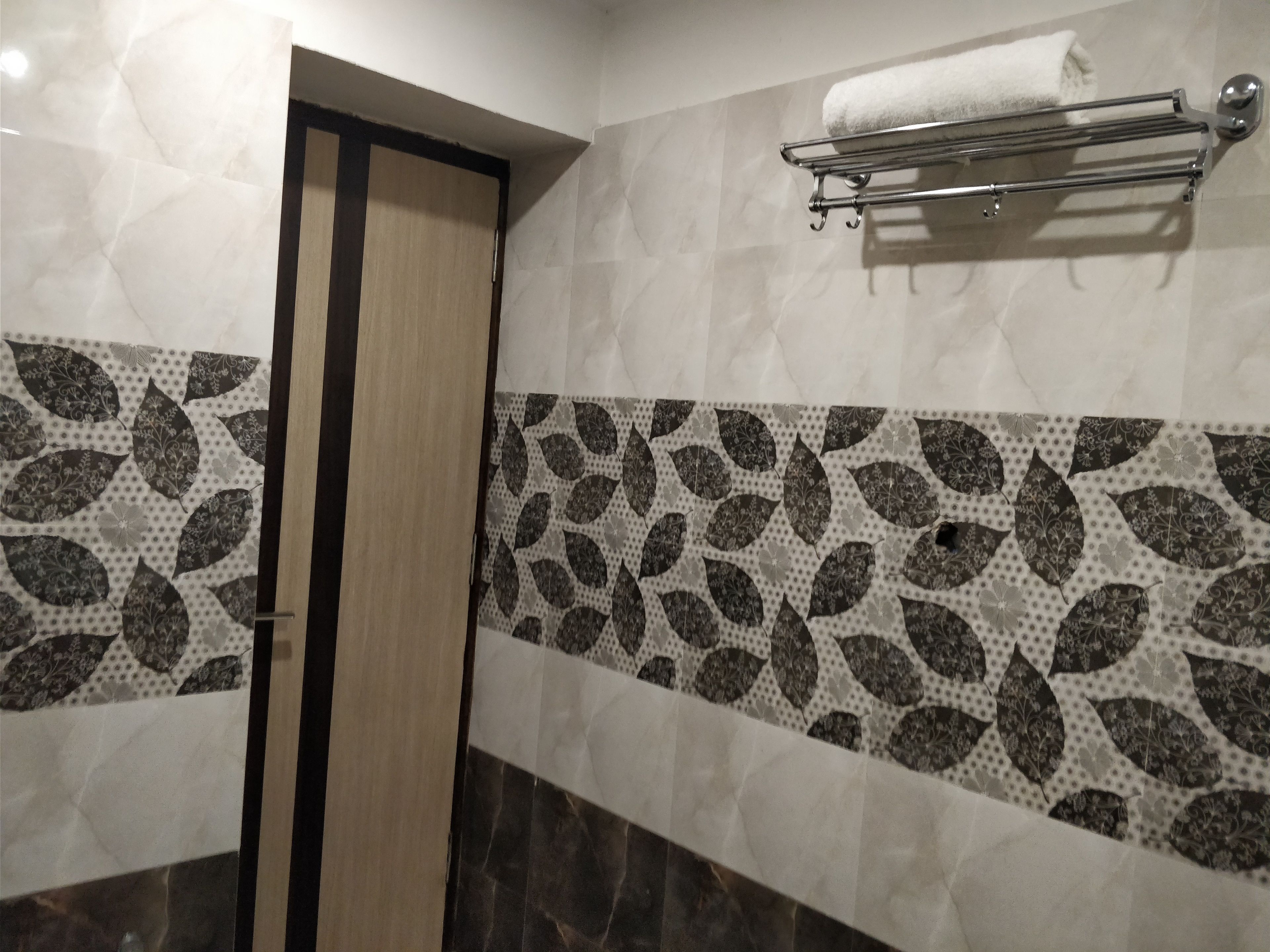Un baño con puerta de madera, un perchero con una toalla blanca y baldosas estampadas.