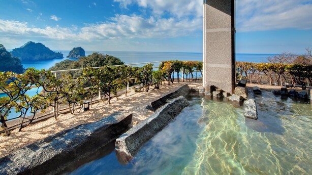 Vista despejada de una piscina con escalones de piedra, cerca de una valla de madera, y una lejana vista del mar y las islas.