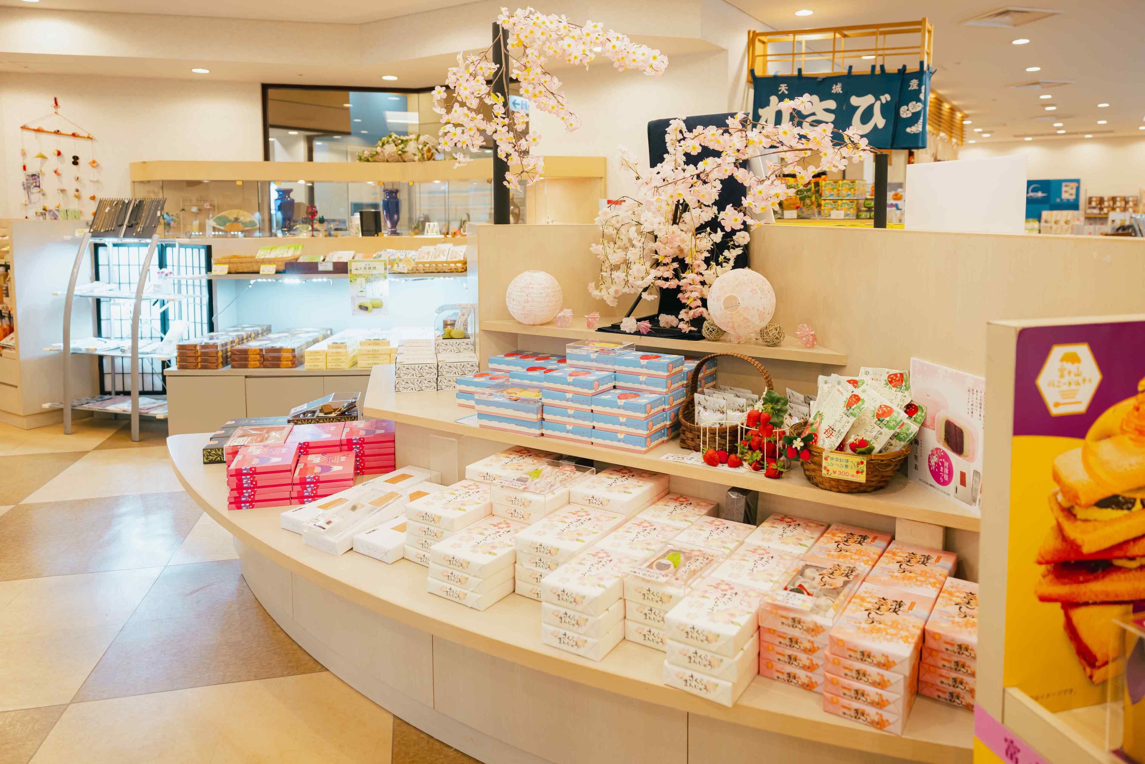 A store interior with shelves of packaged goods, decorative cherry blossoms, and a counter with various items.