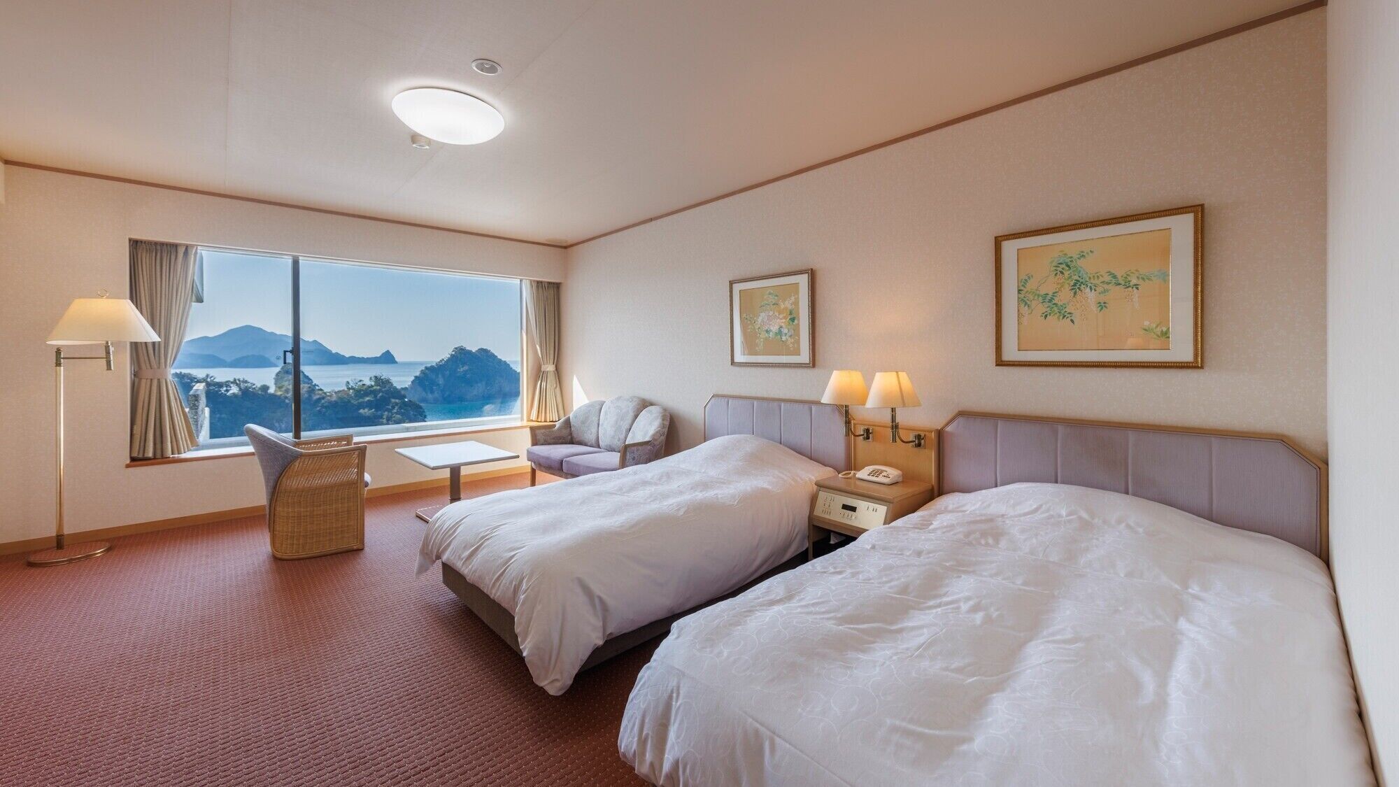Een hotelkamer met twee bedden, een bureau, een stoel, een lamp en een raam met uitzicht.