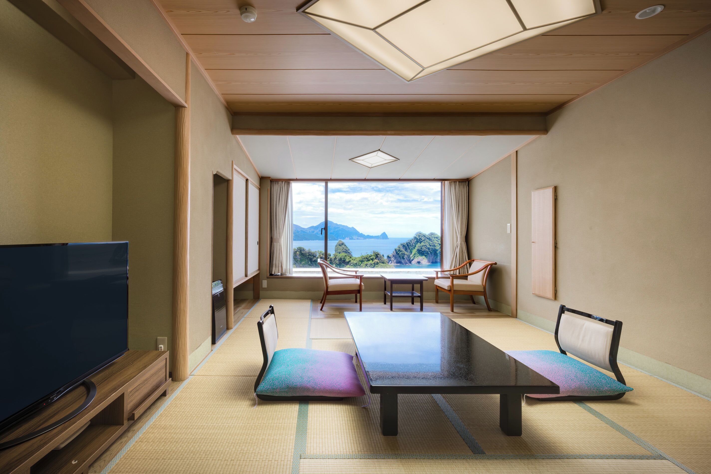 Habitación con televisor de pantalla plana grande, una mesa con sillas y vistas a montañas a través de un ventanal amplio.