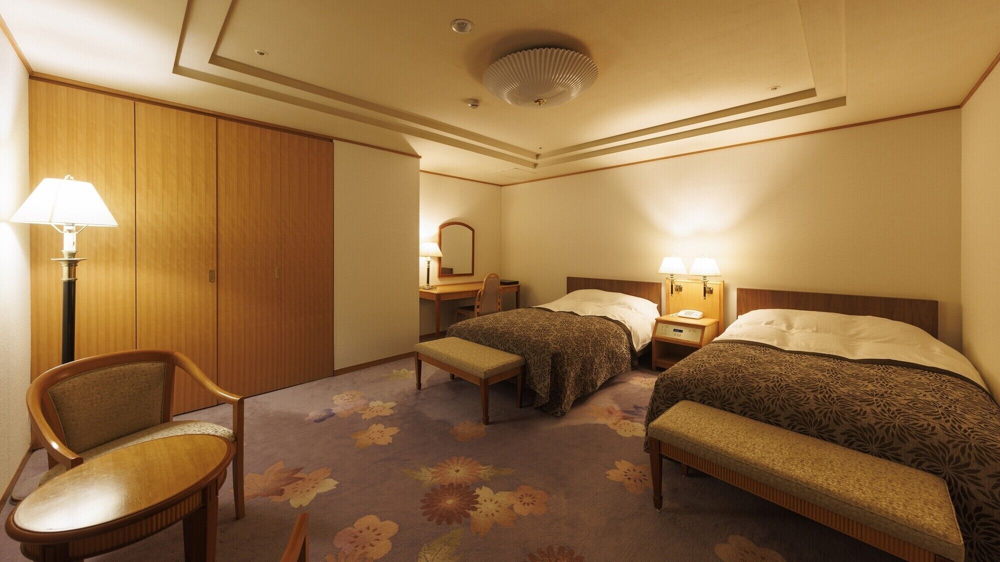 A hotel room with two beds, a desk, a chair, and a wardrobe.