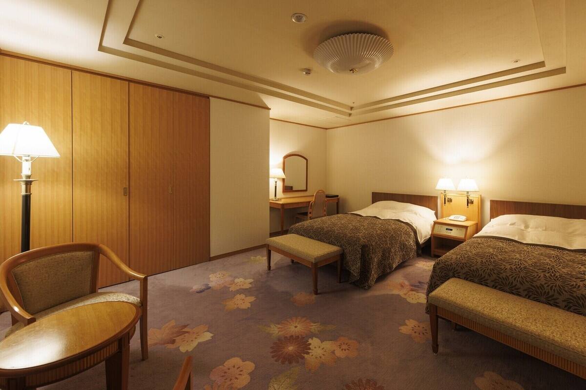 Une chambre d’hôtel avec deux lits, un bureau, une chaise et une armoire.