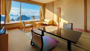 Una habitación con suelo de tatami, una mesa baja, un sofá y un ventanal con vistas al paisaje costero.